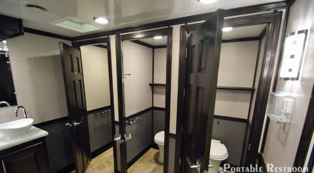 Portable restroom with multiple stalls, dark doors, and a sink visible on the left.