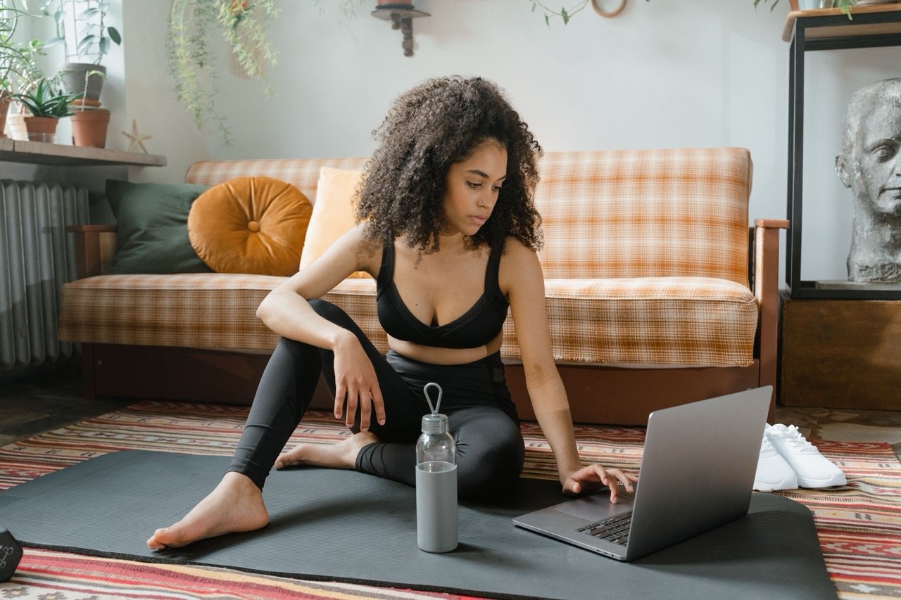 black-woman-sits-on-yoga-mat-with-mac-and-water-bottle.jpeg