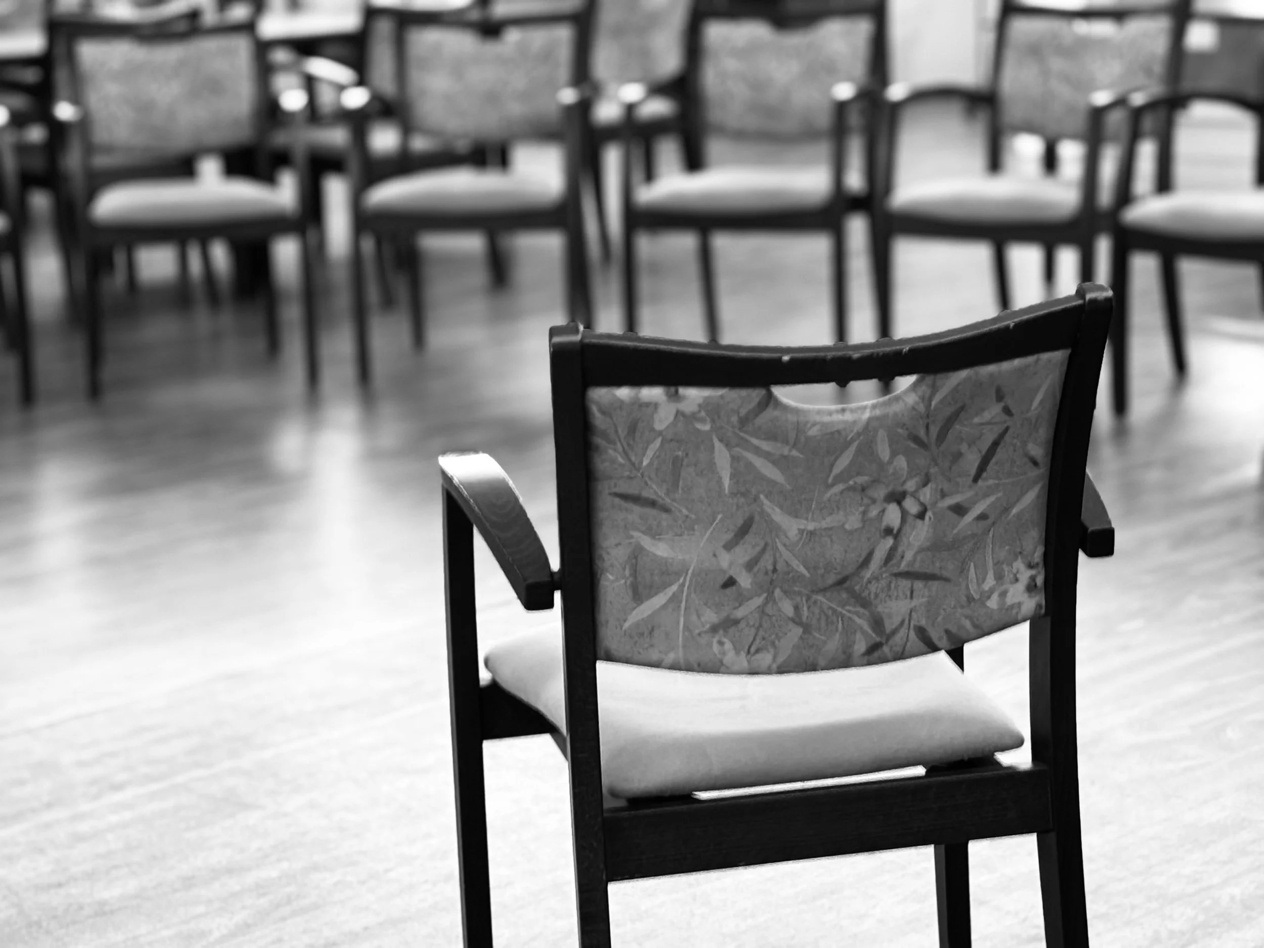 Empty chair with a patterned backrest in a room with multiple chairs in the background.