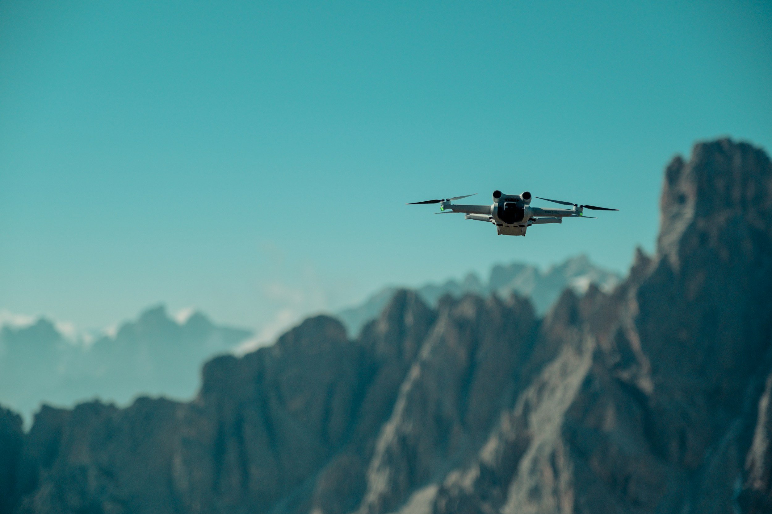 Een drone vliegt boven bergachtige omgeving met rotsen en een heldere blauwe lucht.