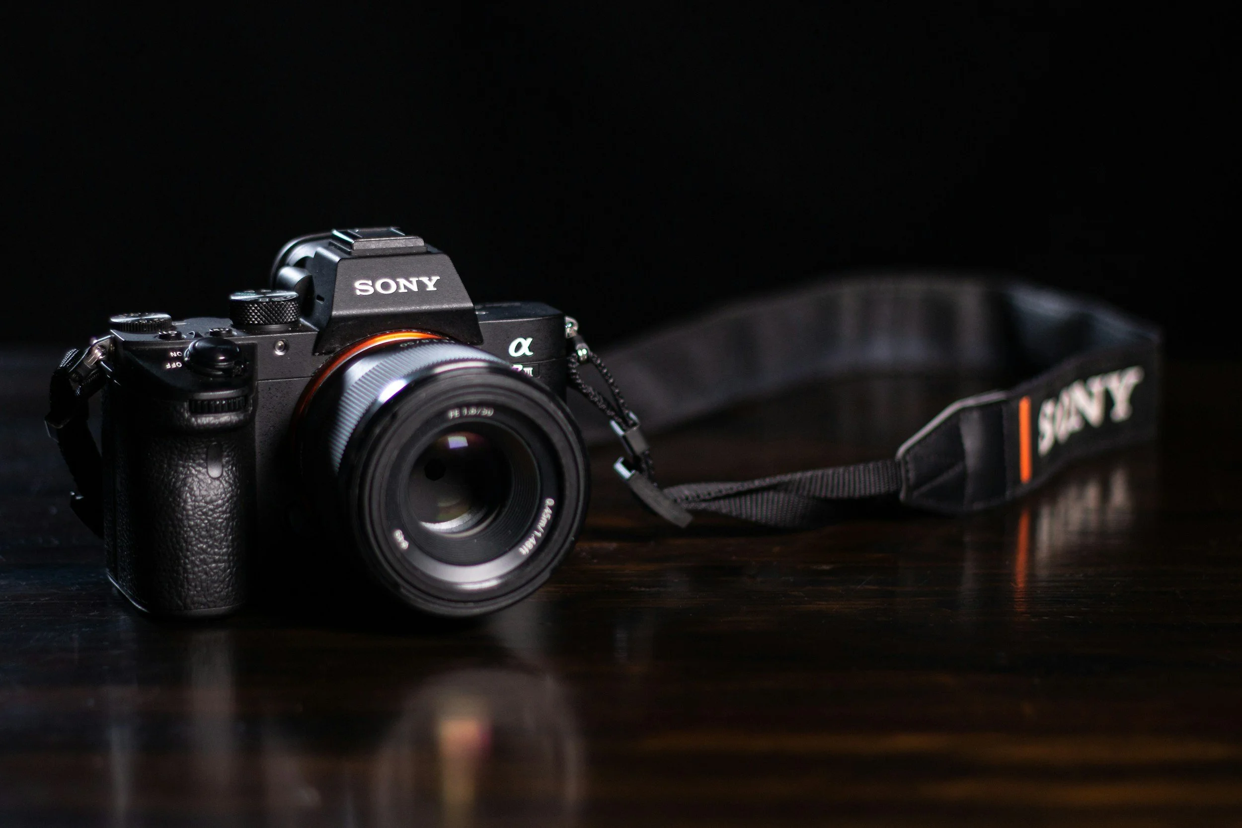Een zwarte Sony camera met een lenselement en een bijpassende draagriem, geplaatst op een donkere houten tafel.