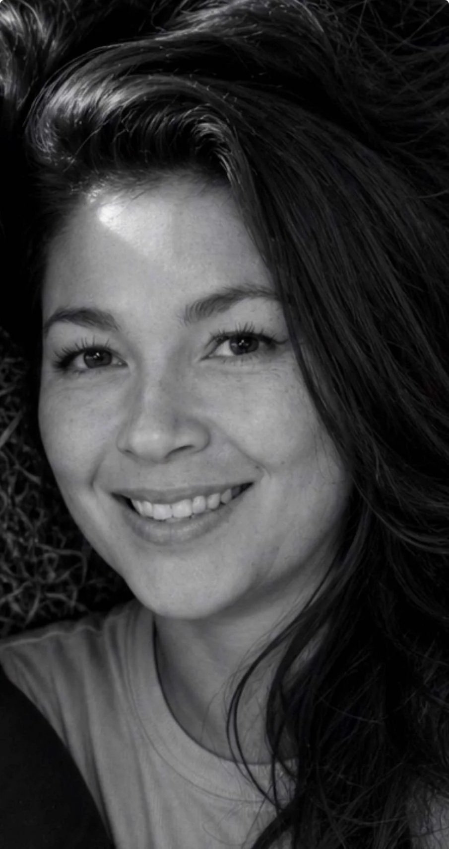 A black and white close-up portrait of a smiling woman with long dark hair.