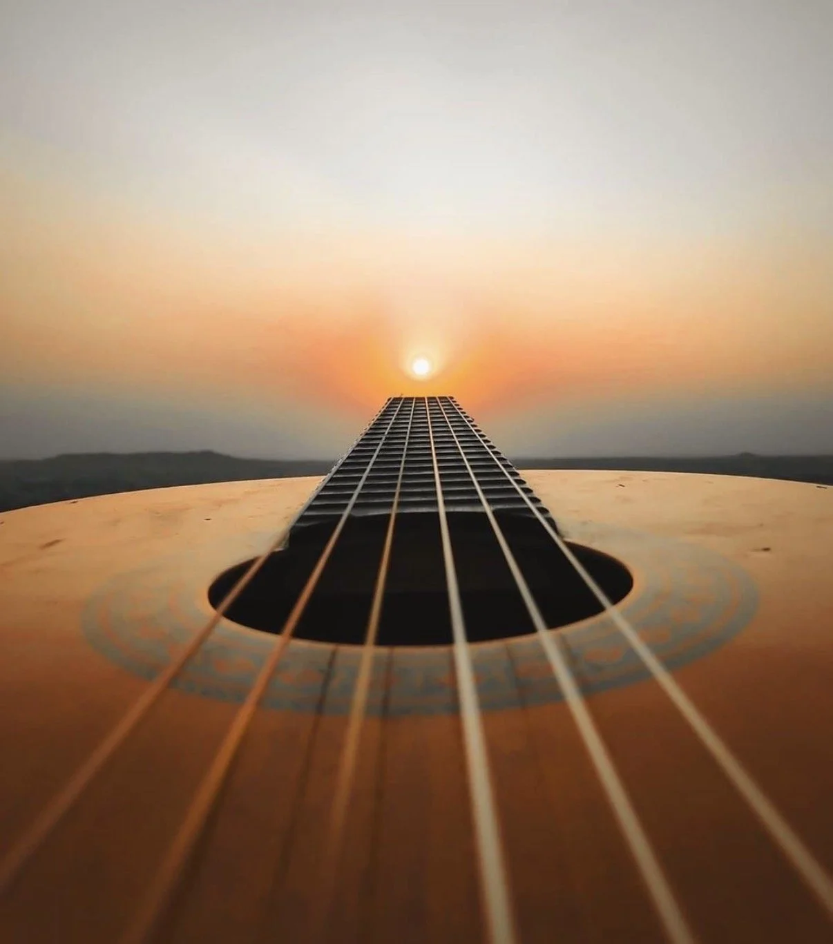 Close-up of an acoustic guitar viewed from the body towards the headstock with the strings leading to a sunset on the horizon.
