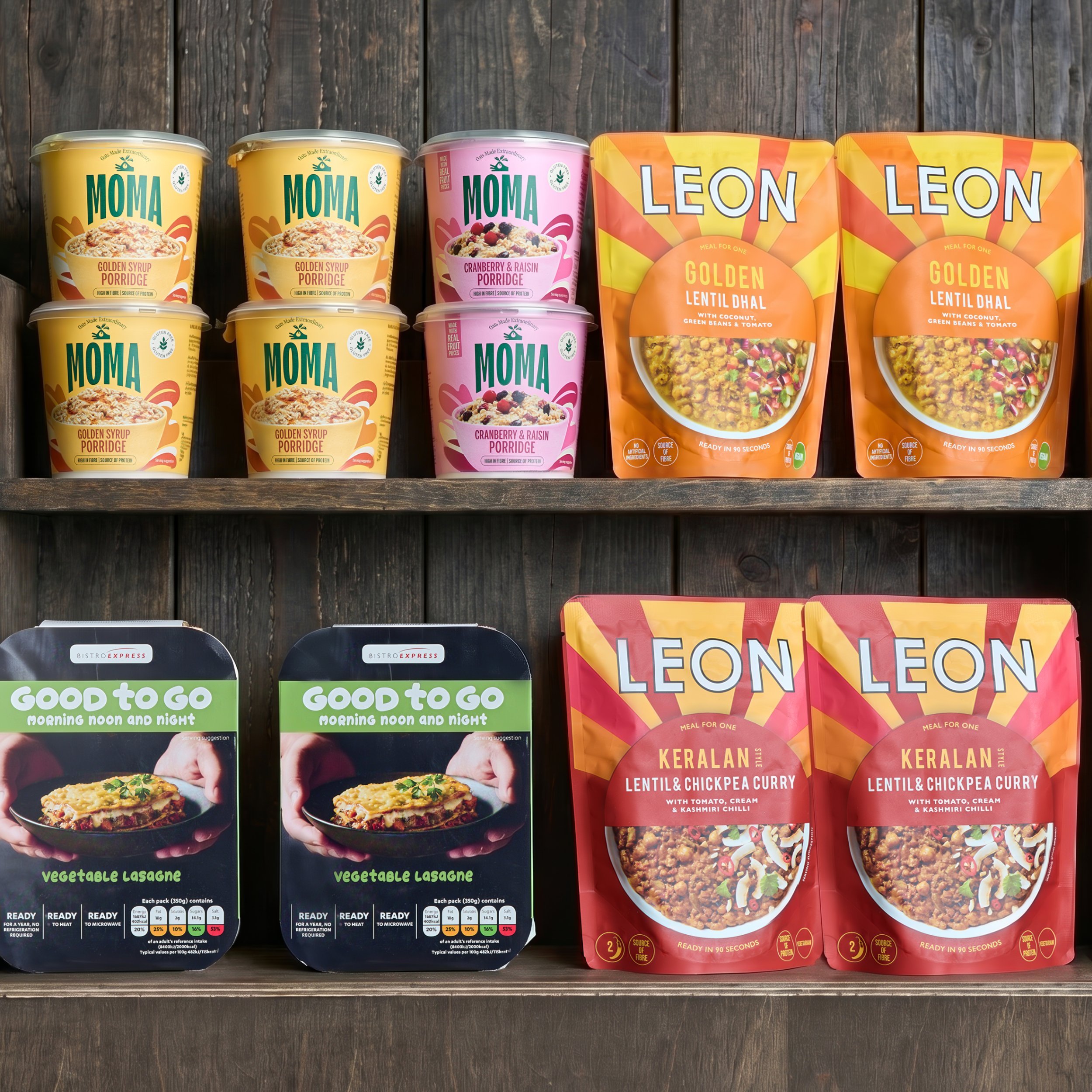 Shelf with various packaged vegetarian and vegan food products, including MOMA porridge with golden syrup and cranberry raisin flavors, and Leon lentil dahl with coconut, green beans, and tomato, on a wooden background.