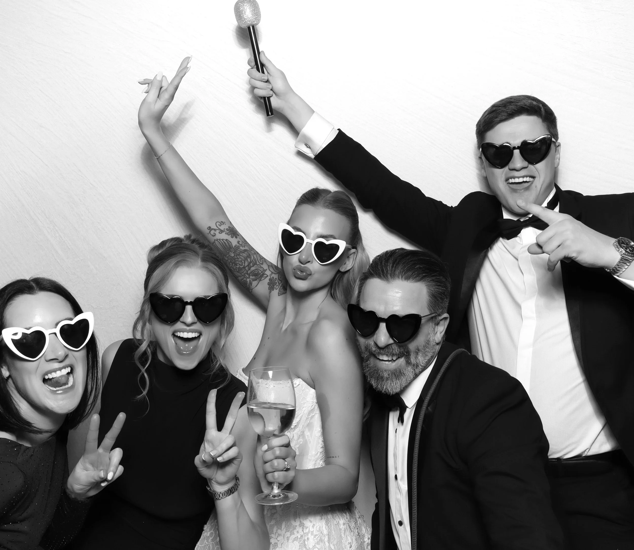 Happy group of people celebrating at a party, wearing sunglasses, holding a toast glass, and making peace signs.