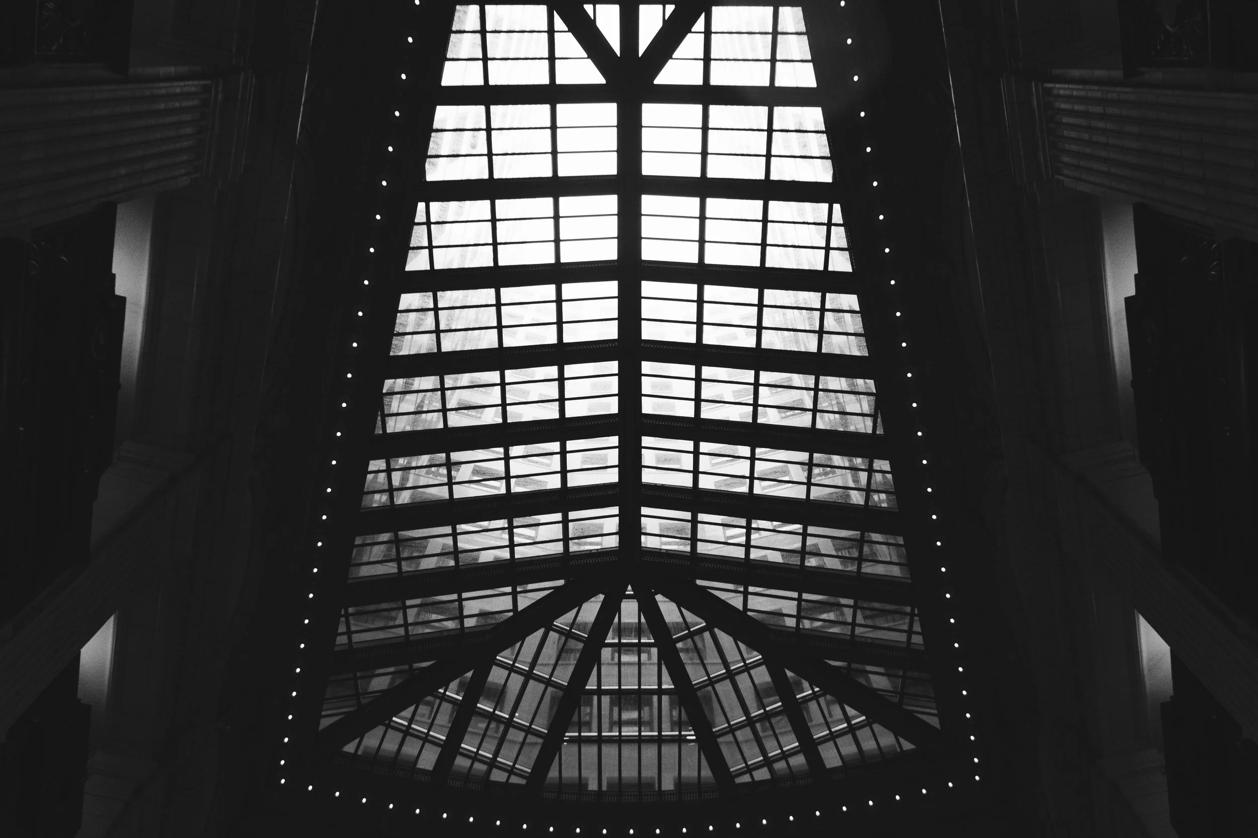 Interior view of a building's glass roof structure with metal framing, silhouetted against the sky.