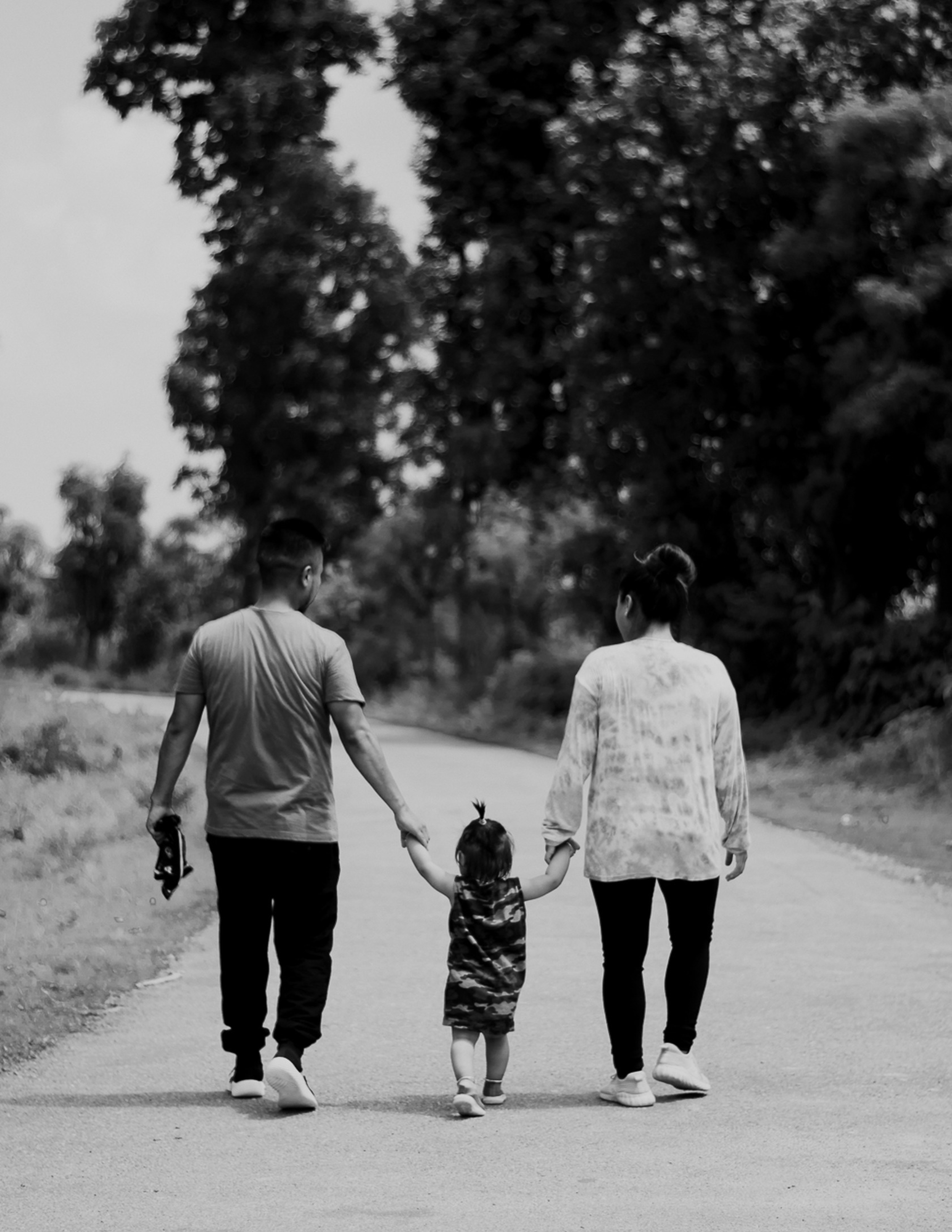 A family walking on a path in a park, holding hands, with trees in the background.