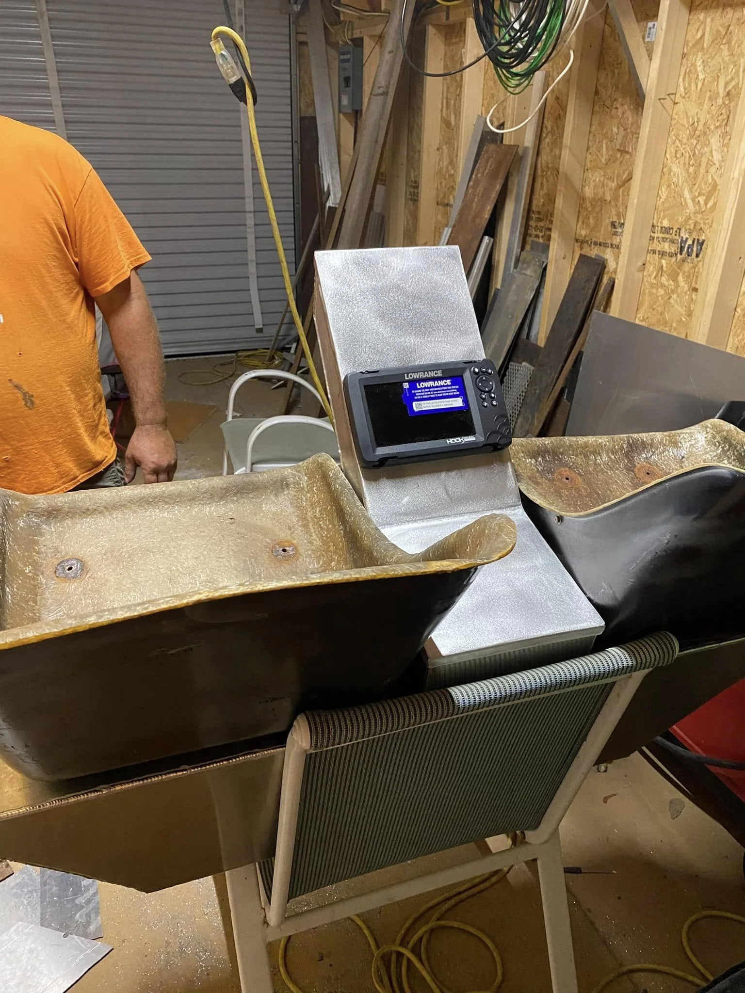 A work space with two bathtubs, a Lowrance fish finder on a table, and some scattered tools and materials on a garage or workshop wall.