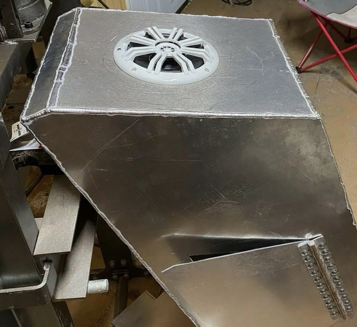A large metal cube with a speaker mounted on the top surface, situated in an industrial setting.