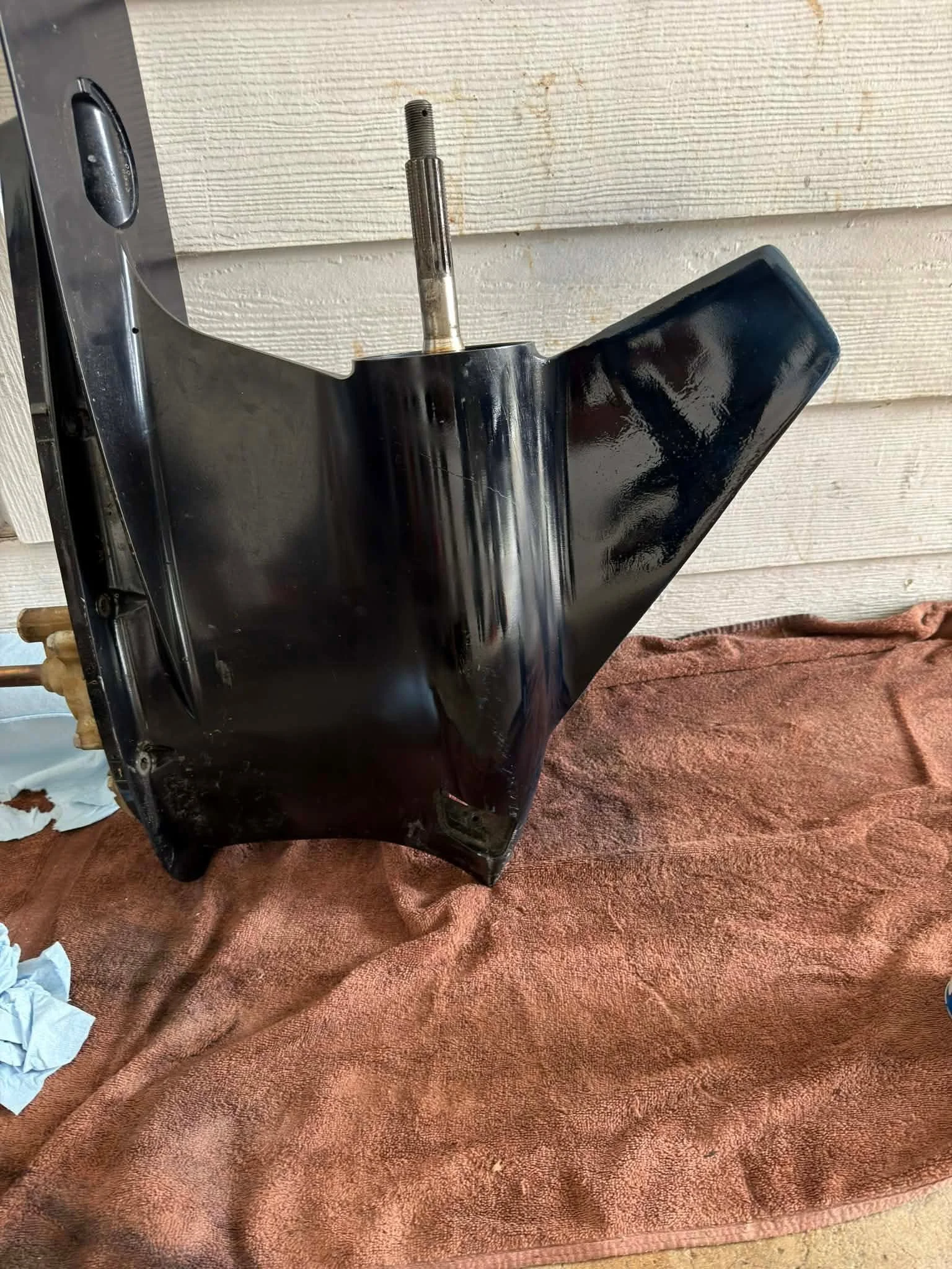 A black automotive part, possibly a bumper or panel, mounted on a brown cloth on the ground with a textured white wall in the background.