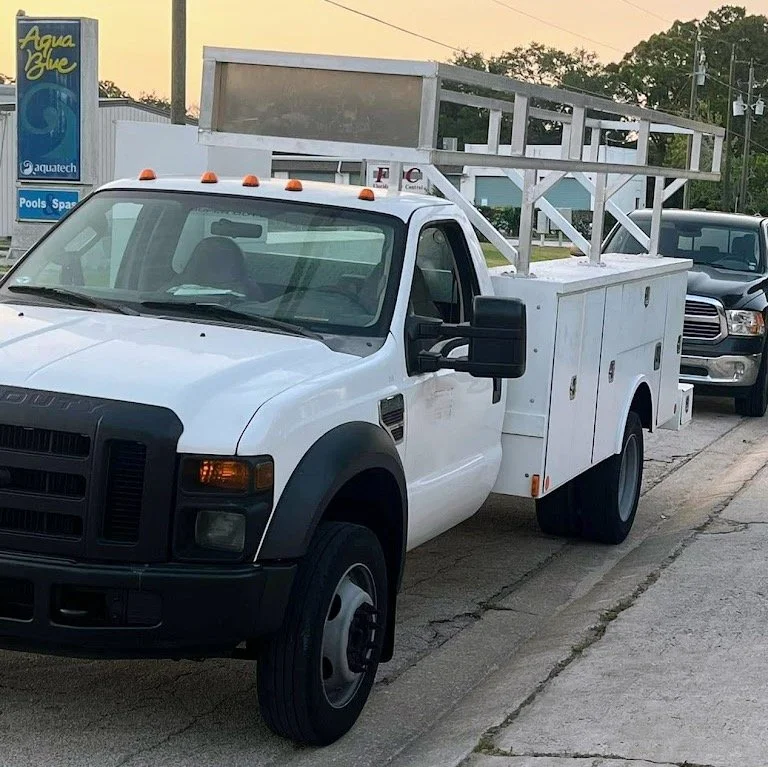 A white utility truck with a ladder on top parked on the street.