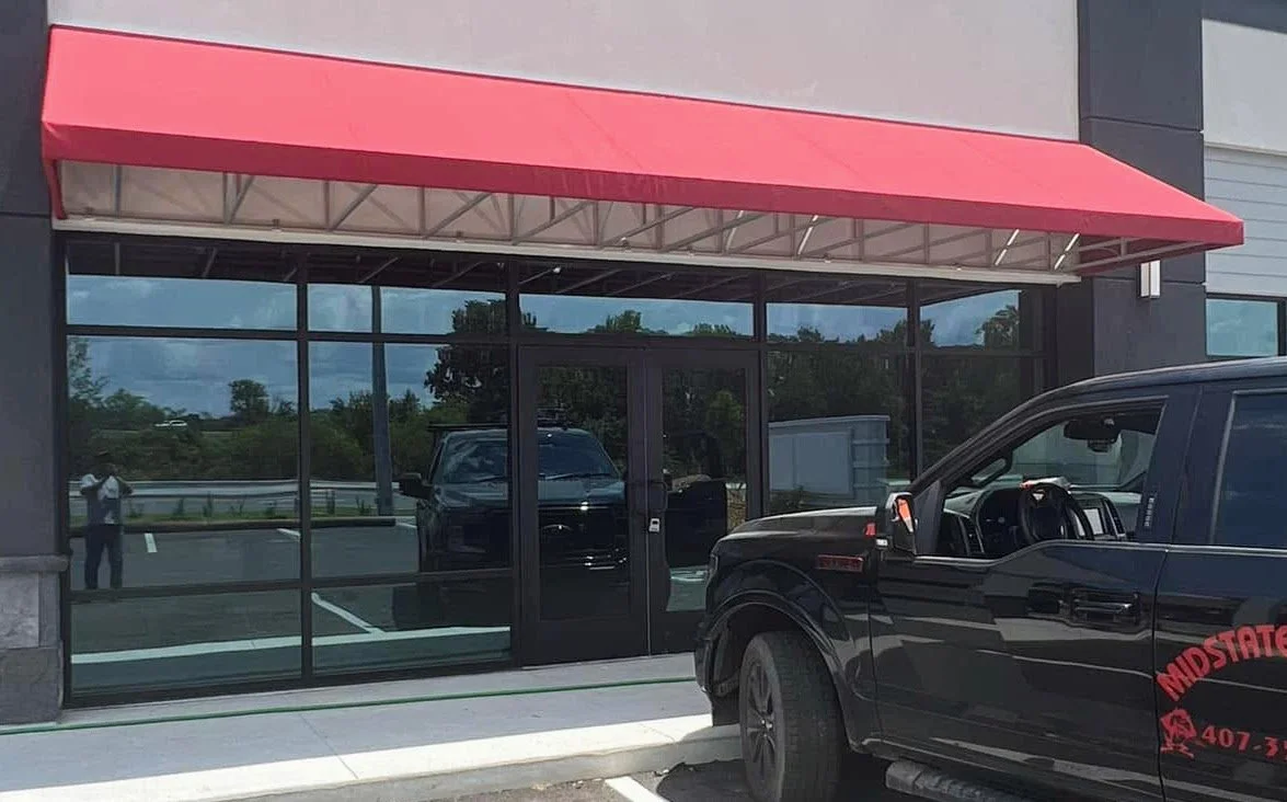 Exterior of a commercial building with large glass windows, a red awning, and a black pickup truck parked outside.