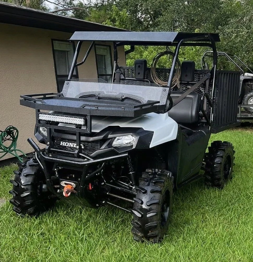 A black and white Honda with off-road tires parked on a grassy lawn, with a house and trees in the background.