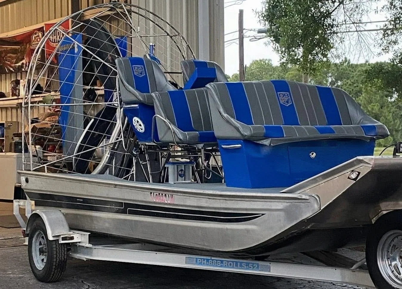 A hovercraft with blue and gray seats on a trailer in a warehouse with tools and shelves in the background.