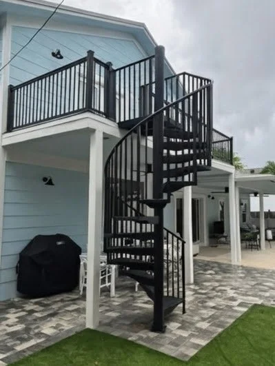 Black spiral staircase outside a light blue house with a balcony.