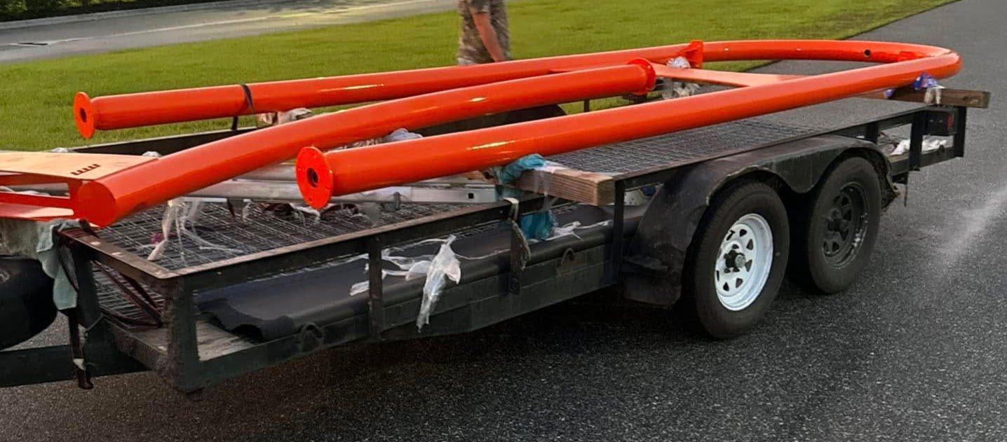 Trailer loaded with orange poles on a paved road.