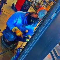 A person wearing a blue jacket and yellow gloves working on maintenance or repair in a workshop.
