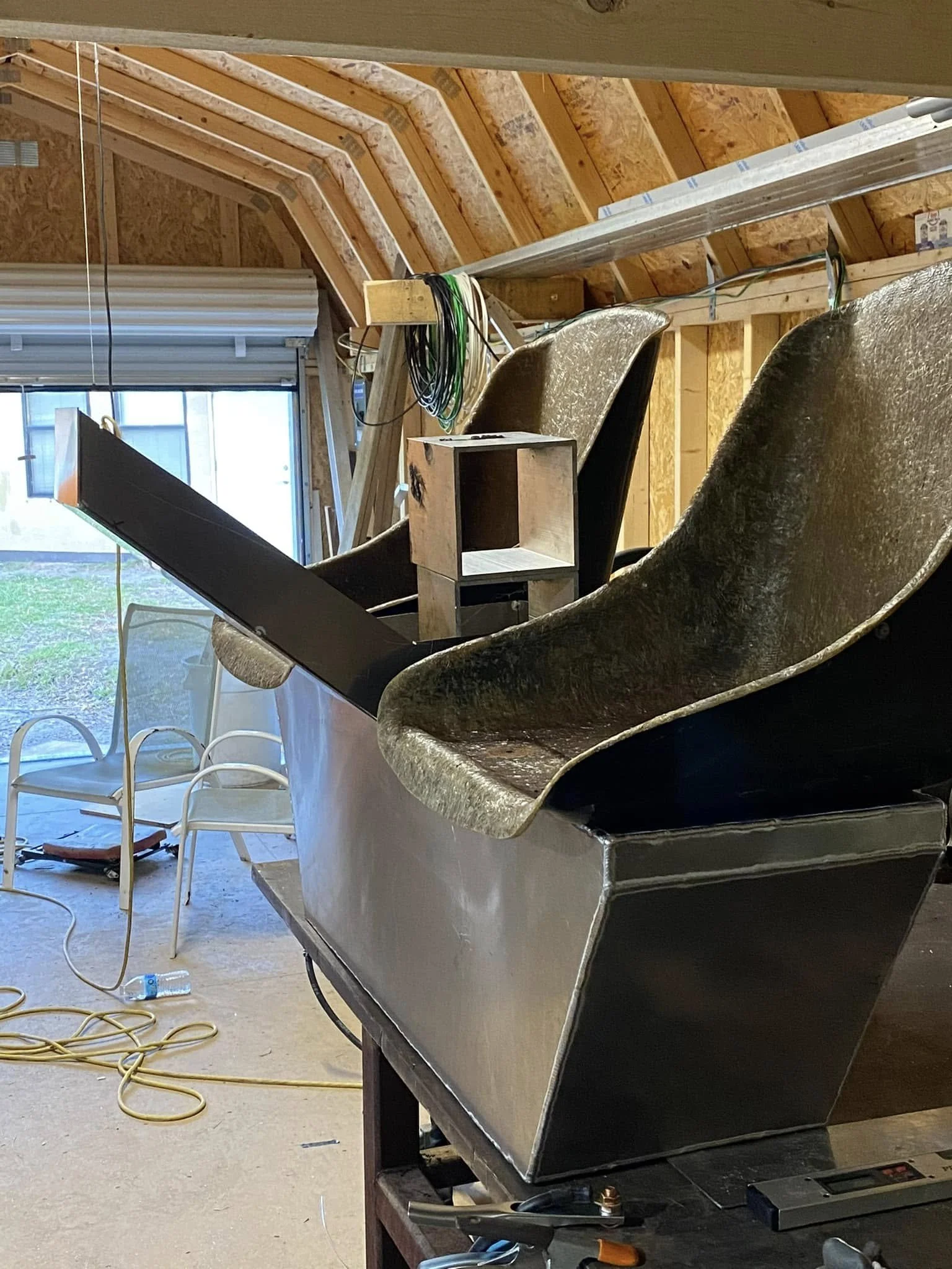 The image shows a construction or renovation scene inside an attic or loft space. There are wooden framing and insulated panels, with some electrical wiring and tools scattered around, including a pair of scissors, a screw gun, and a hole saw.