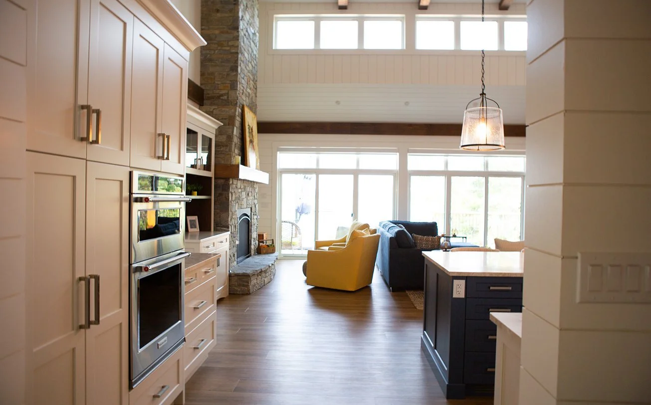 Open-concept living room and kitchen with large windows, a stone fireplace, yellow and black sofas, a kitchen island, and high ceilings