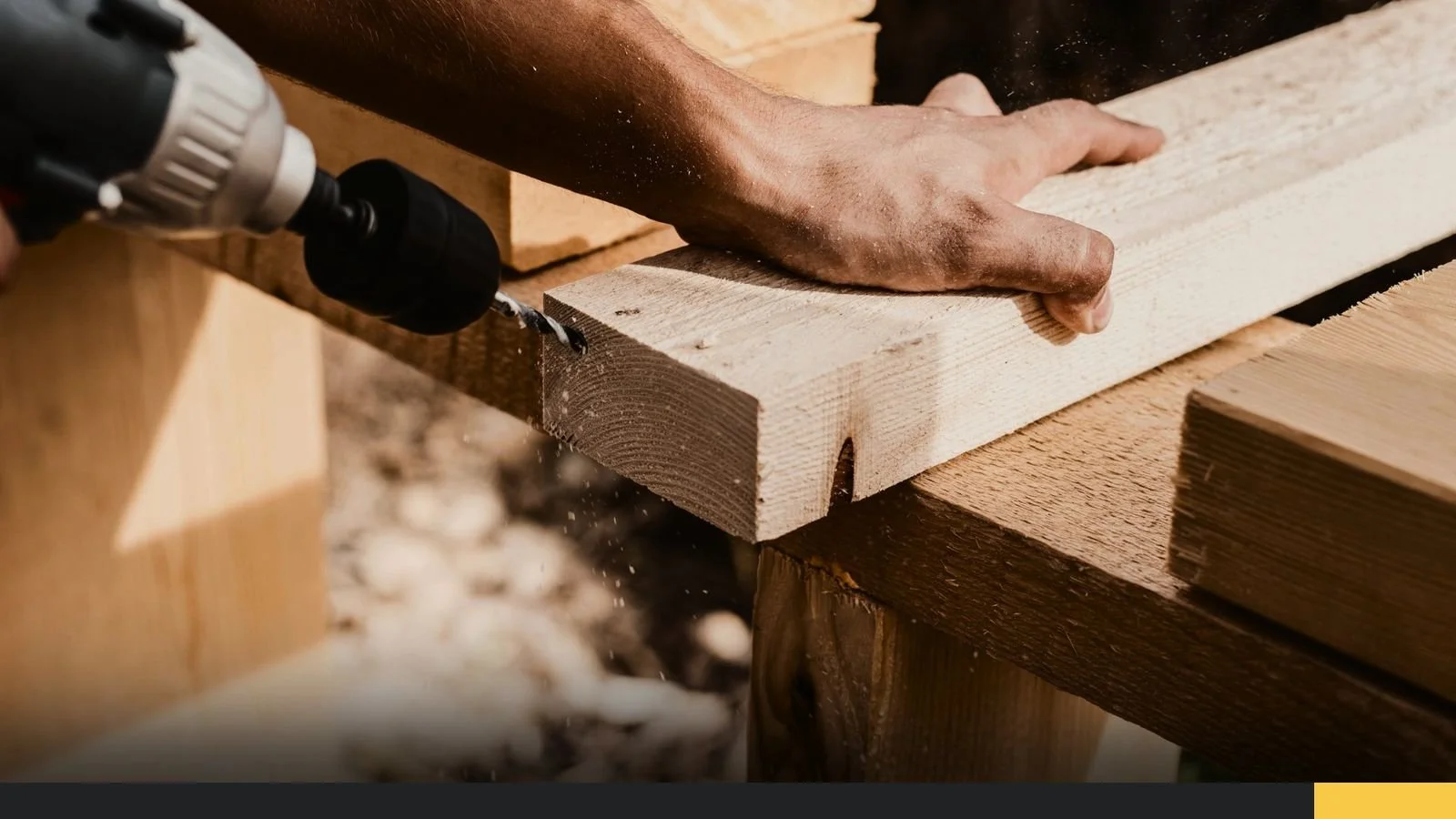 A person using a drill to screw a wooden plank onto a wooden structure outside.
