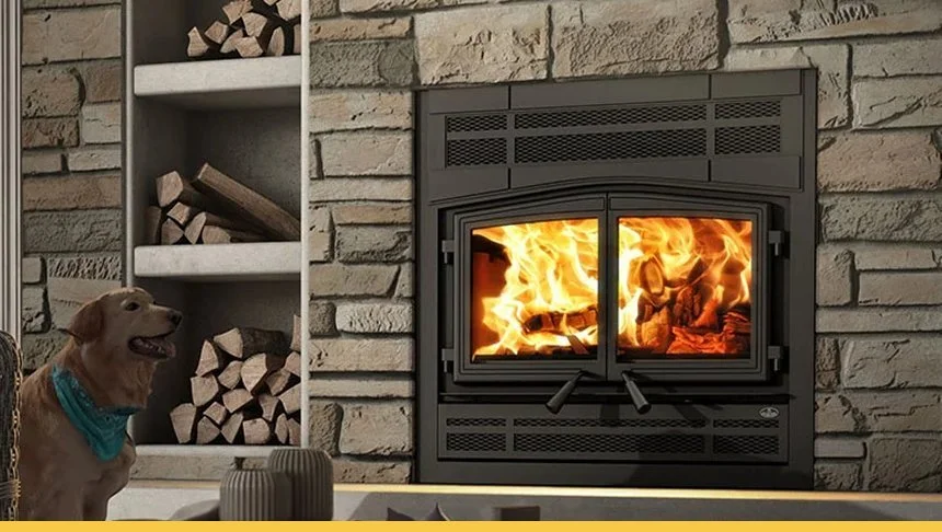 Interior of a living room with a lit fireplace set in a stone wall, a Labrador retriever wearing a blue bandana sitting nearby, and a shelf with stacked firewood.