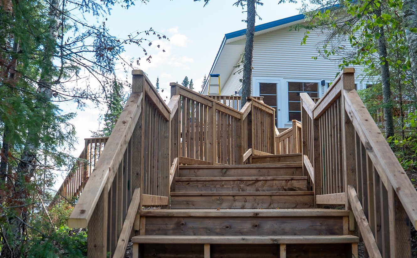 Wooden staircase leading up to a house in a forested area with trees and greenery on both sides.
