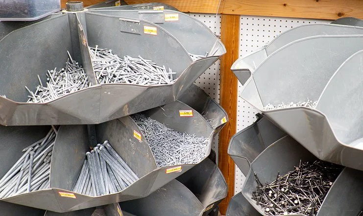 Metal hardware items such as nails, screws, and bolts in large metal bins displayed in a store.