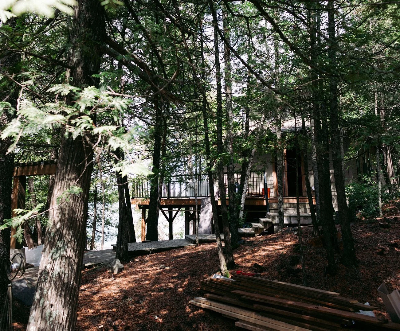 A house under construction in a wooded area, with stairs and a deck being built among tall trees.