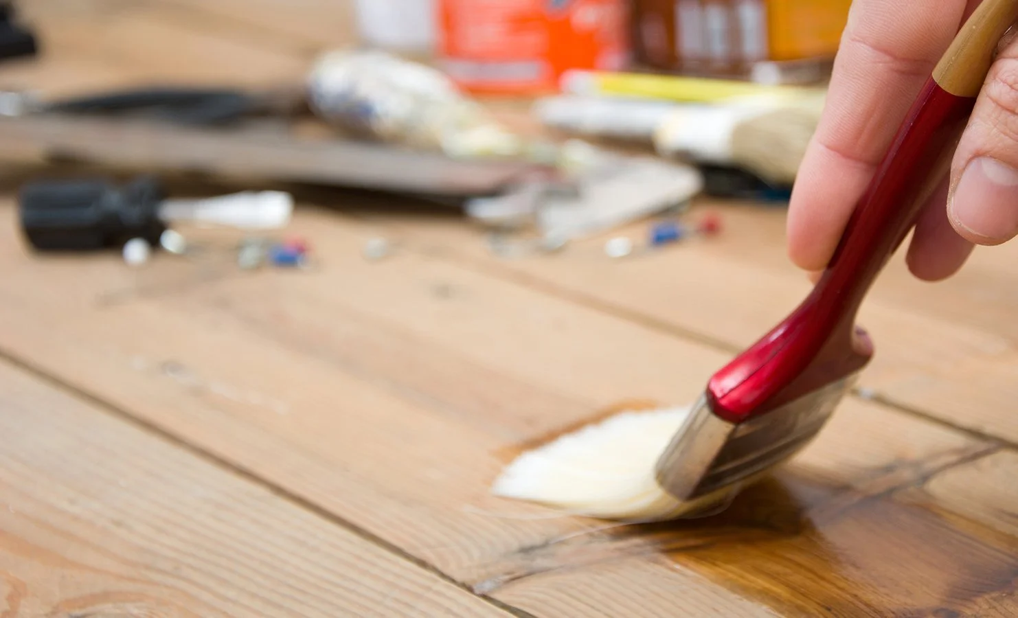 Close-up of a person's hand applying a wood stain or varnish to a wooden surface using a paintbrush.
