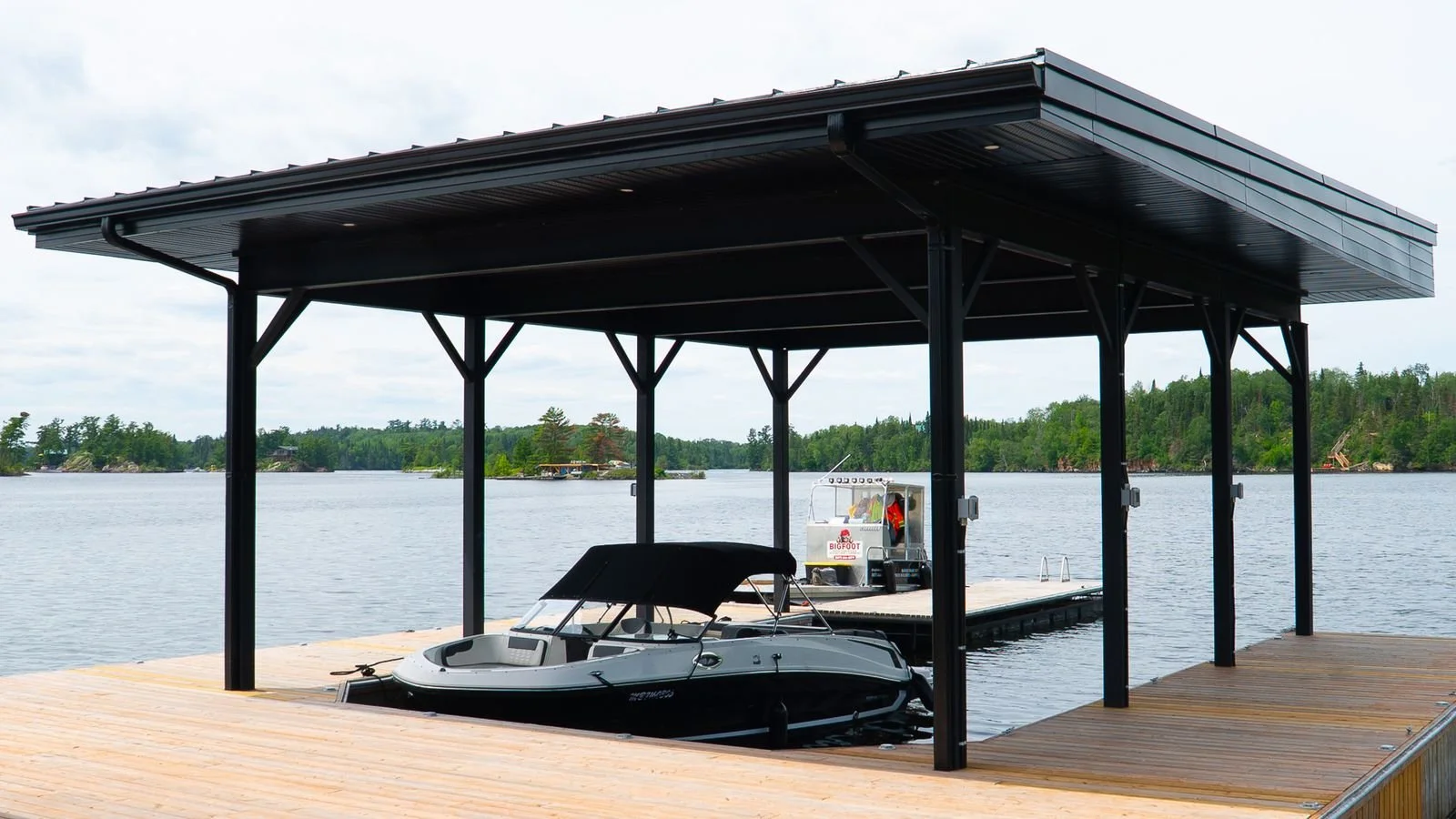 Dock with a boat and a covered shelter on a lake with trees in the background.