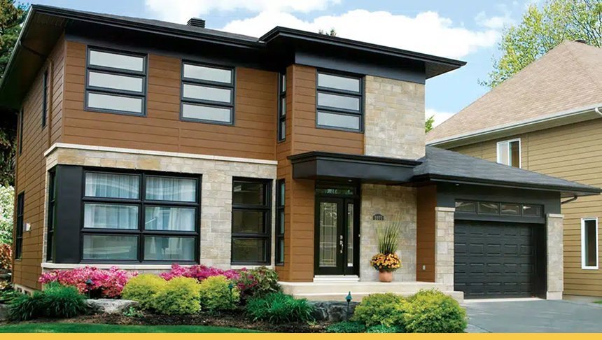 Modern two-story house with a combination of wood and stone exterior, large front windows, a black garage door, and landscaped front yard with colorful flowers.
