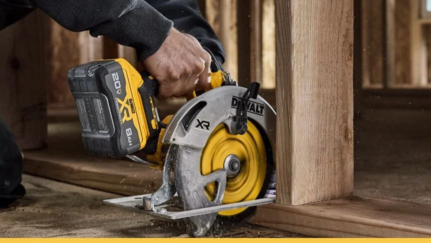 Person cutting a wooden board with a yellow cordless circular saw at a construction site.