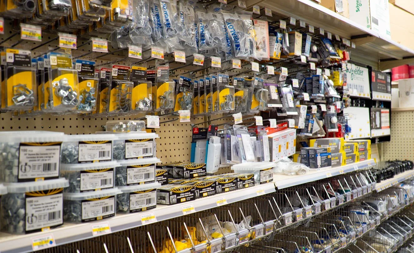 A hardware store aisle with shelves loaded with various hardware items such as bolts, nuts, screws, and other fasteners, organized in plastic packaging and small boxes.