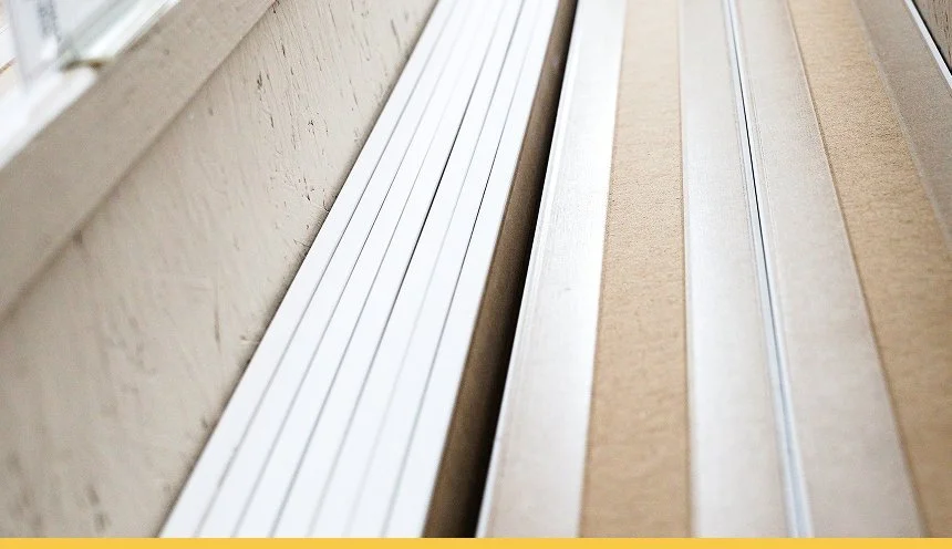Close-up of white and beige window sills with metal tracks, viewed from inside a room.