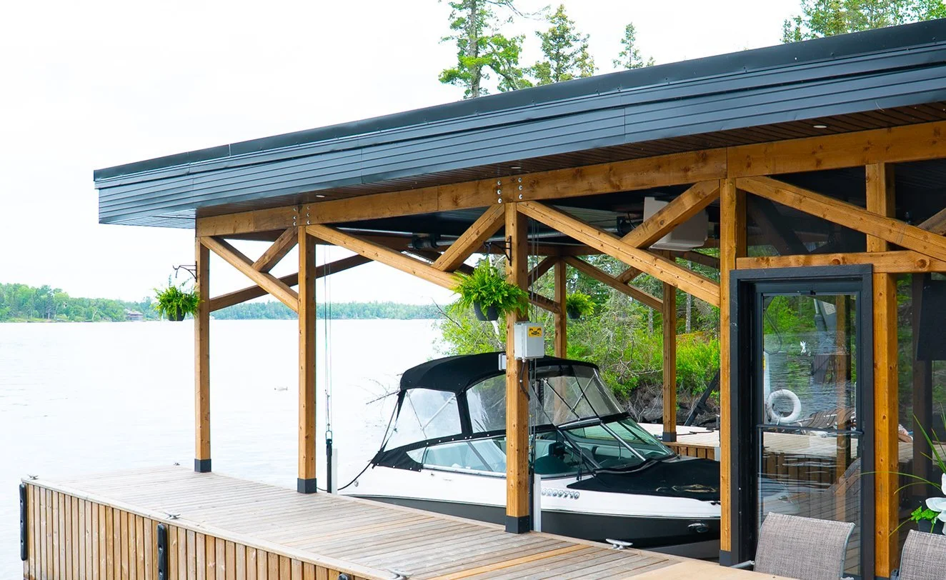 A modern lakeside boathouse with a boat docked inside, surrounded by greenery and water.