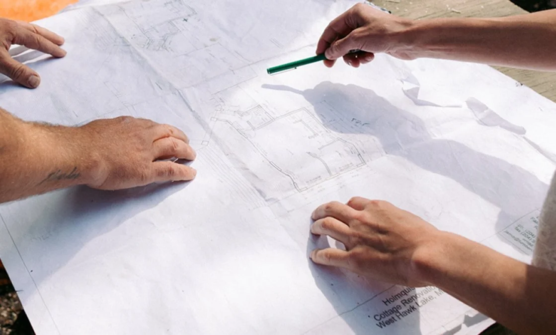 Two people looking at a large architectural blueprint spread out on a table, with one person holding a green pen.