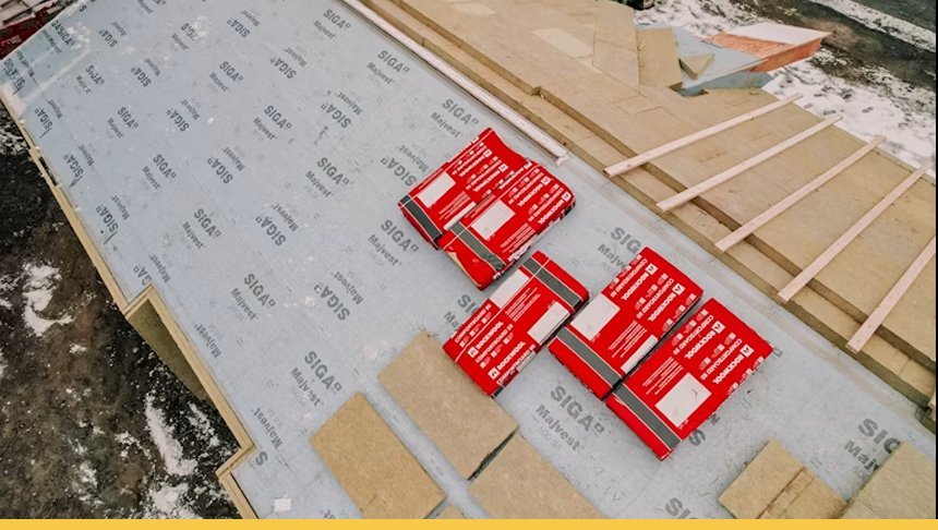 Construction site with insulation, plywood, and framing materials on a snowy ground.