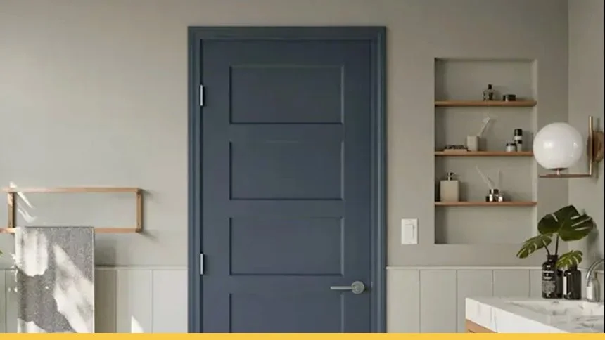 Interior view of a stylish bathroom with a blue door, a built-in shelved niche, a round wall-mounted light, a green plant, and a marble countertop with black bottles.