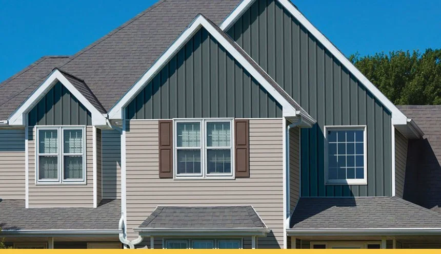Close-up of a modern house with blue and beige siding, multiple windows with shutters, and a gray shingled roof.