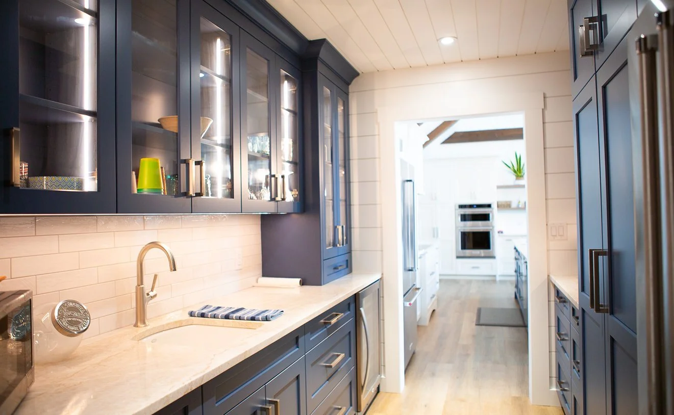 Modern kitchen with blue cabinets, beige countertop, white subway tile backsplash, stainless steel fixtures, and hardwood flooring. Bright and airy with visible appliances and decorative items.