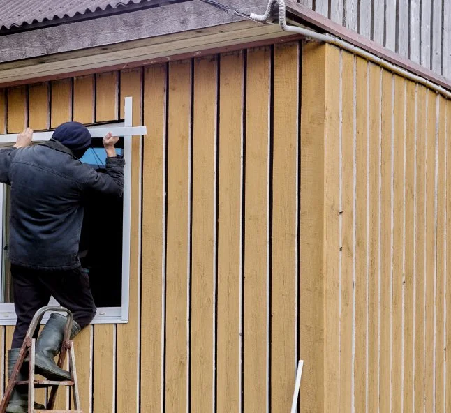 Person installing window trim on the exterior of a wooden building