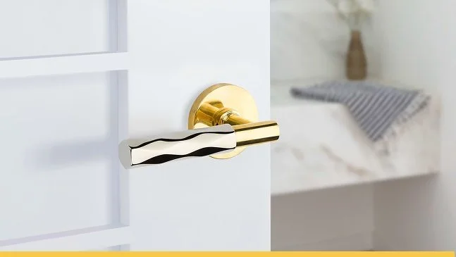 Close-up of a door handle with a gold base and a uniquely shaped silver lever.