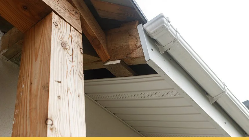 Close-up of a house roof with a wooden support beam and white gutter system attached to the roof's edge.