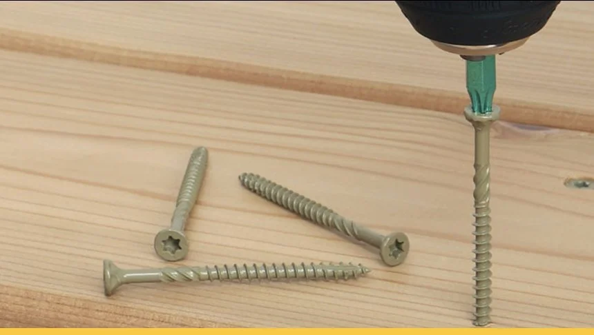 A power drill inserting a screw into a wooden surface, with three additional screws lying on the wood nearby.
