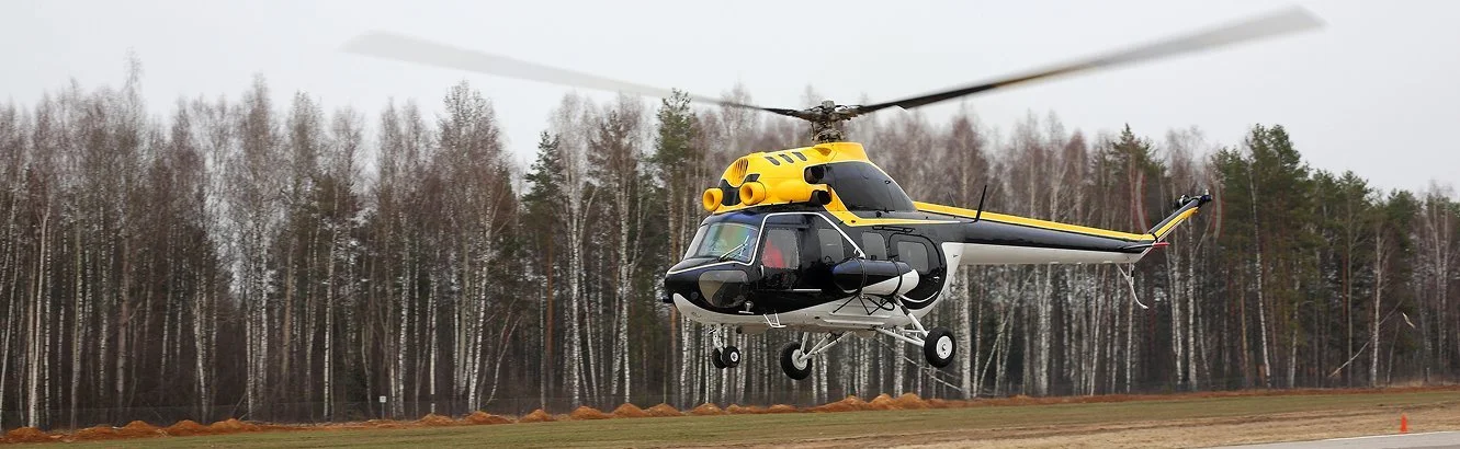 A black and yellow helicopter hovering just above the ground in an open field with trees in the background.