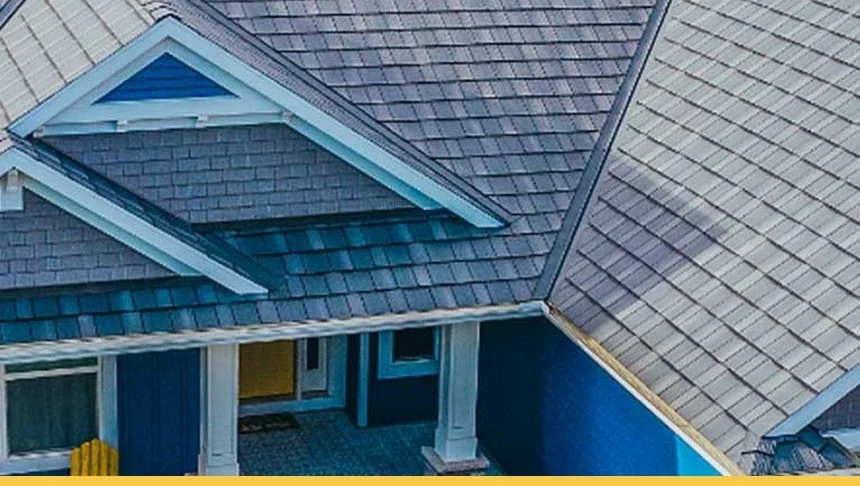 Aerial view of a house with gray shingle roof and blue siding, showing a dormer window and part of a front porch.