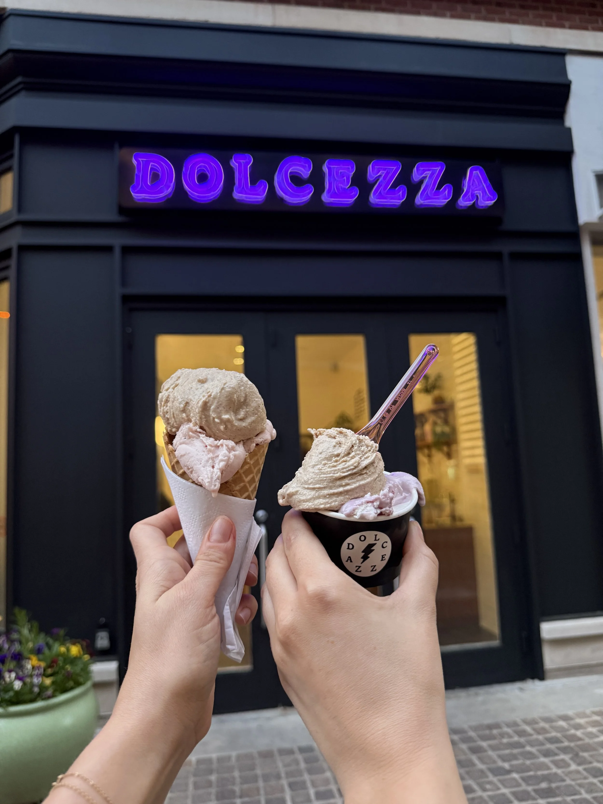 People holding up two ice cream desserts in front of store Dolcezza.