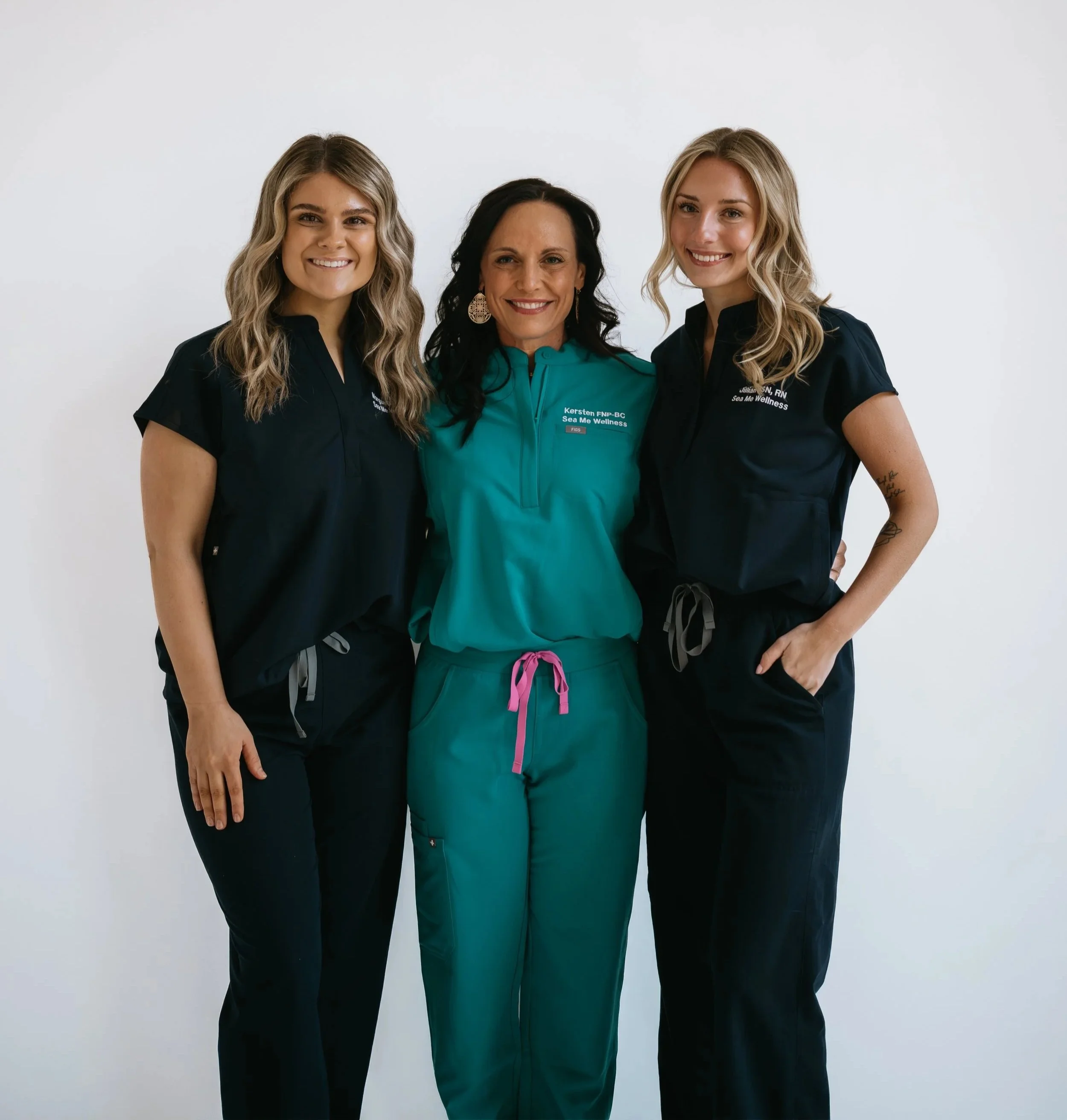 Three Sea Me Wellness team members in medical scrubs smiling together.