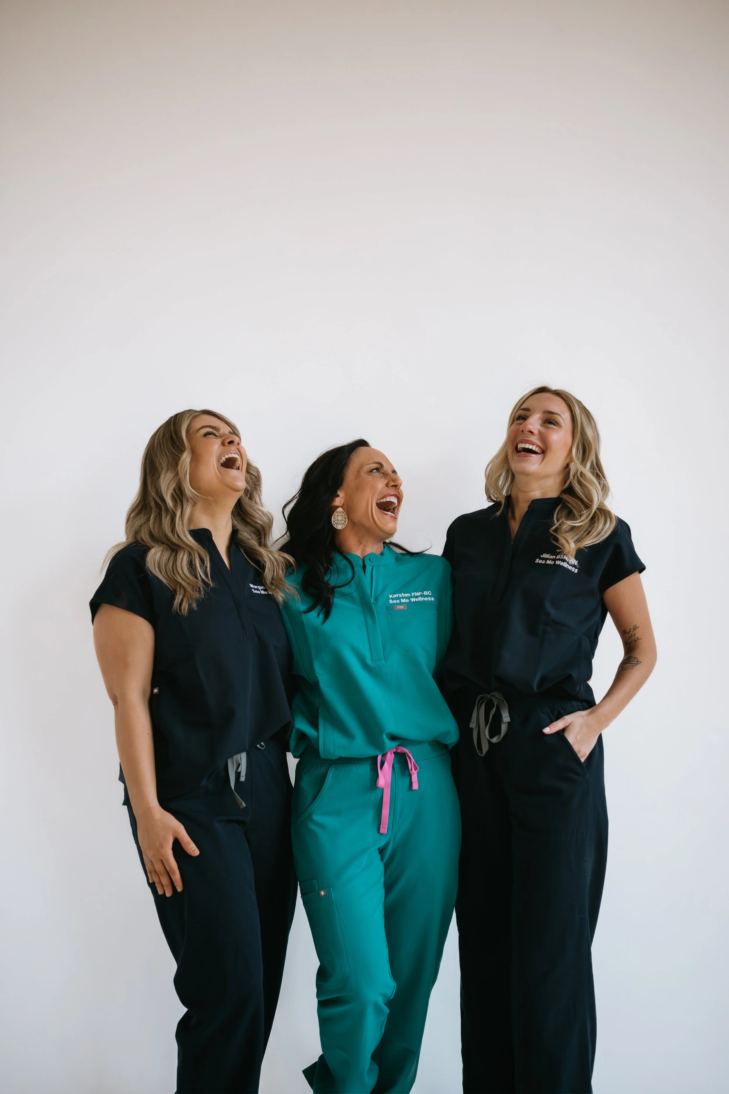Three Sea Me Wellness team members laughing together in medical scrubs.