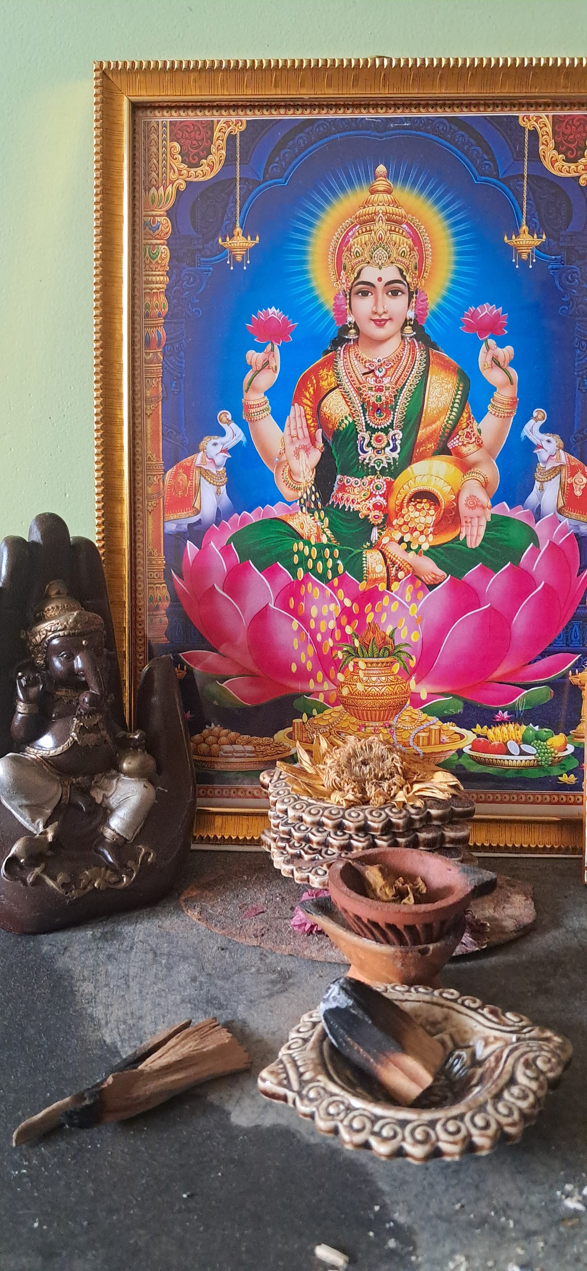 Hindu altar with a framed picture of goddess Lakshmi, surrounded by offerings, incense, and statues.